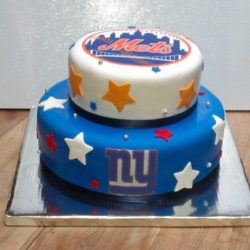 A two-tiered cake decorated with sports team logos is the centerpiece of our bakery café. The top tier features a white base with the New York Mets logo and vibrant star decorations, while the bottom tier boasts a blue base with the New York Giants logo and matching stars. All this sits elegantly on a silver board.